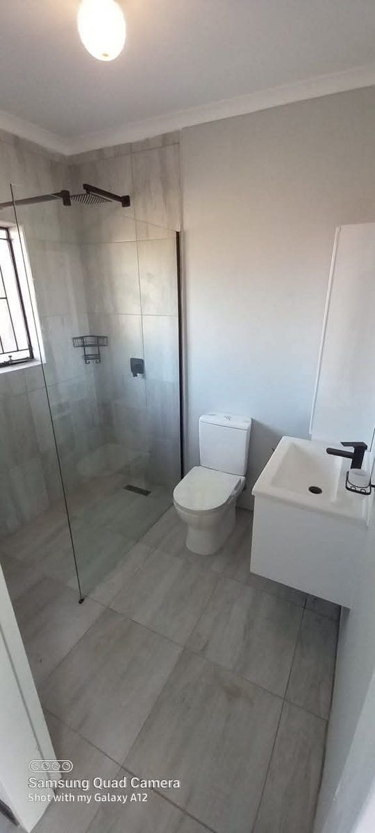 Glass shower enclosure with toilet and wall-mounted sink after Sphapower Plumbing renovation