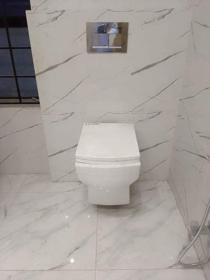 Wall-mounted toilet installed in a marble-tiled bathroom by Sphapower Plumbing